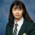 Zhifan Ye - Teenage girl with dark hair wearing green blazer and tie in front of blue background