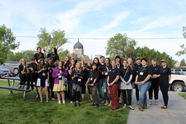 Large group of people wearing black t-shirts standing in front of trees and domed building