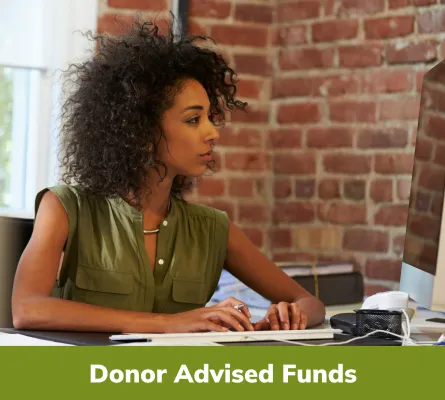 Donor Advised Funds - Woman working on a computer in front of a brick wall