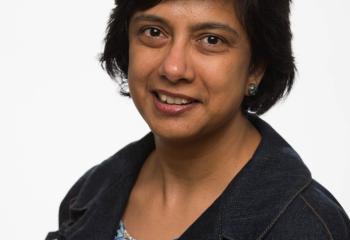 woman with short, dark hair, wearing denim jacket and multi-colored shirt