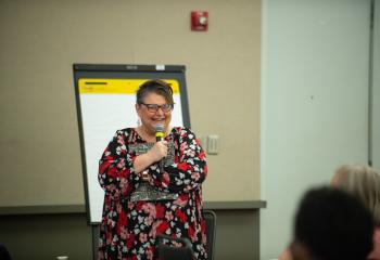 Jen Stancil - woman smiling and holding a microphone wearing a floral dress