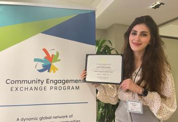 Gulan Gawdan - Woman holding certificate in front of banner that says Community Engagment Exchange Program