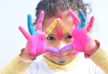 Young girl with paint on her hands holding her fingers in a triangle shape