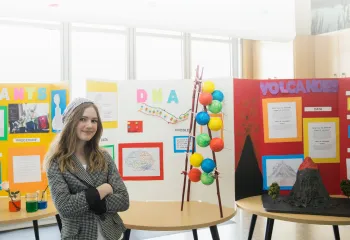 A girls posing for a photo in front of her science fair projects