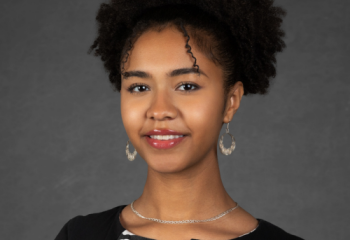 Jamora Arroyo Jefferson - Young woman with curly black hair in front of a gray background