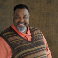 Man wearing orange shirt with brown striped sweater vest