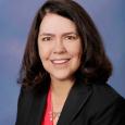 Sharon Schendel - woman wearing black blazer and pink shirt in front of blue background