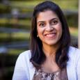 Munira Tayabji - woman with dark hair wearing a brown shirt and white cardigan sweater