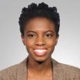 Randi Williams - woman with short, black hair wearing a brown jacket in front of a gray background