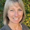 Kim Collazo Headshot - woman with blond hair and gray jacket in front of greenery