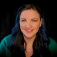 Kiki Prottsman - woman with long, dark hair wearing a green shirt in front of a blank background