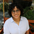 Woman with short, dark, curly hair wearing a blue button up shirt