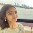 Neha Shahi - young woman with dark hair sitting in a boat with water and cityscape behind