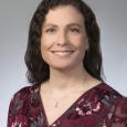 Holly Woodward Ballard - woman with long, dark hair wearing burgundy floral top in front of gray background