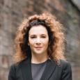 Madeline Di Nonno  - woman with curly brown hair wearing black blazer and gray shirt