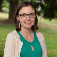 Emily Coyle - Woman with short brown hair wearing glasses and green shirt with tan sweater