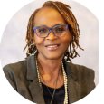 Sheila James - woman with brown hair in locs wearing gray blazer and pearl necklace