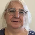 Brenda Stanley - Woman with white hair and glasses wearing a blue shirt