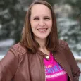 Sara Kobilka - woman with brown hair wearing a pink shirt and brown leather jacket