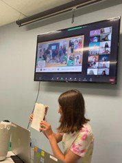 Tenn girl holding up a notebook with a Zoom meeting image on the screen behind her